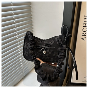 Detalle del bolso plisado negro con textura floral y colgante de corazón decorativo