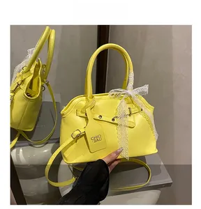 Detail view of yellow leather handbag featuring a white lace bow and decorative buckle