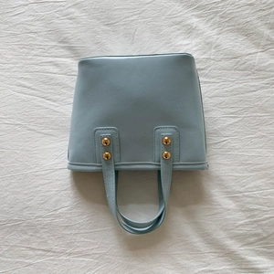 Close-up of light blue leather bucket bag with elegant gold rivet handle hardware