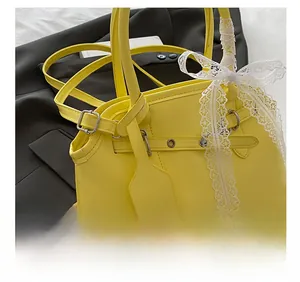Detail of yellow square tote bag featuring a white lace bow and branded leather tag