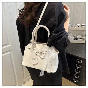 Detail of white leather handbag featuring delicate lace bow and polished texture finish