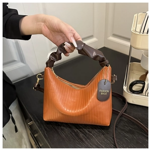 Detail of caramel orange pleated cloud bag featuring soft dark coffee handle and gold hardware
