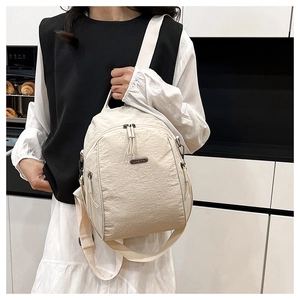 Close-up of cream textured nylon backpack with metal zipper and brand plaque on a model