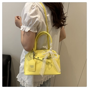 Detail of yellow shell bag with white lace bow and branded tag on white lace top