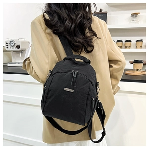 Close-up of a black nylon backpack with metal logo detail in a modern cafe setting