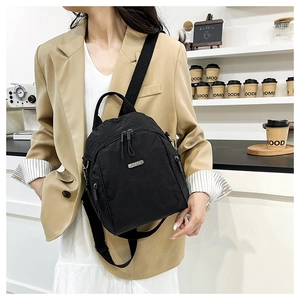 Detail of black nylon crossbody bag with multiple zippers and silver logo in a cafe setting