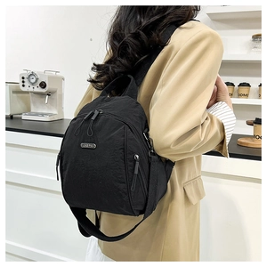 Detail of a black nylon mini backpack featuring a metal logo plate and smooth zip closures