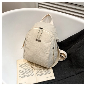 Detail of a cream nylon backpack showing textured fabric and JINGPIN metal logo plate