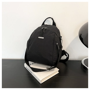 Close-up of black nylon backpack with silver logo plaque and dual zipper compartments