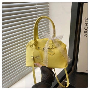 Dettaglio di una borsa squadrata giallo brillante con fiocco in pizzo bianco e manico tondo