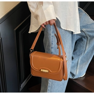 Detailed view of the caramel brown leather crossbody bag featuring a gold cylindrical clasp