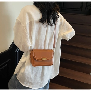Brown leather crossbody square bag with gold cylinder buckle shown on a model