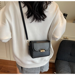 Detail of black leather crossbody bag featuring a golden cylindrical swivel lock and stitching