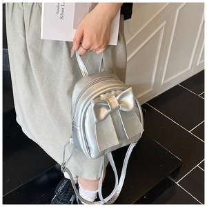 Detail view of a silver mini backpack with a large decorative bow and metallic finish