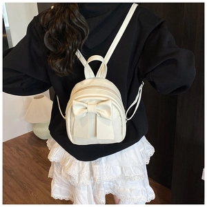 Detail of a creamy white mini backpack with a large bow on model in casual wear