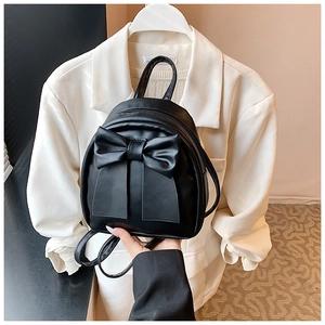 Detail of a chic black mini backpack featuring a large decorative bow and shiny PU leather finish