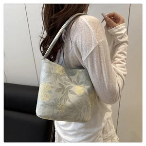 Detail of light grey-green tote bag with yellow floral patterns worn by a model