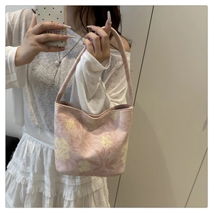 Detailed embroidery on floral pink bucket bag held by model with white dress
