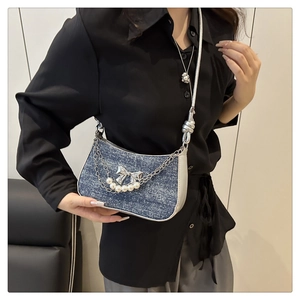 Detail of denim crossbody bag with silver bow, pearl chain and knotted shoulder strap