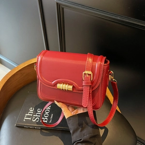 Chic red faux leather square crossbody bag with gold cylindrical lock on a dark chair