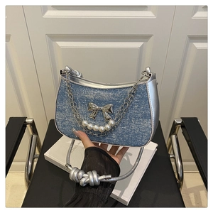 Detail of blue denim shoulder bag with silver bow, pearl chains, and metallic strap