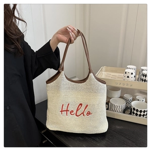 Detail of cream straw tote with red 'Hello' embroidery and brown leather handles