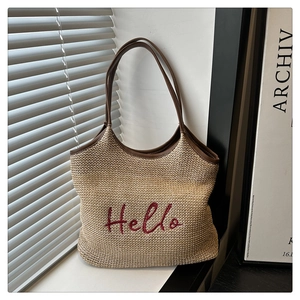 Detail of red Hello embroidery on beige straw tote bag with brown leather handles