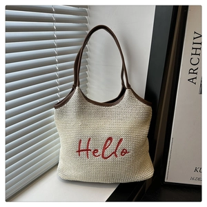 Detail of cream woven tote bag with red Hello embroidery and brown leather shoulder straps