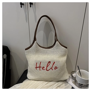 Detail of woven beach tote featuring red Hello embroidery and brown leather handle