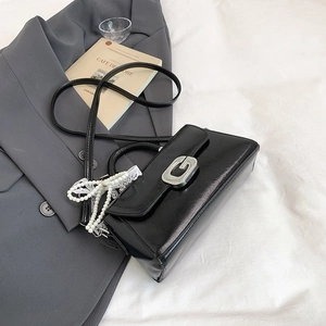 Detail of black glossy leather handbag with silver G-buckle and pearl lace bow charm