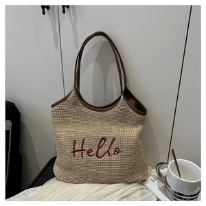 Detail of handwoven straw tote with red Hello embroidery and brown leather handles