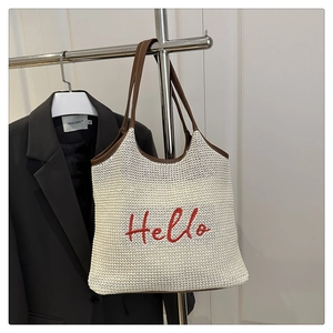 Detail of woven straw tote bag featuring red Hello embroidery and brown leather handles