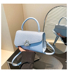 Close-up of light blue crossbody bag with herringbone texture flap and heart metal buckle