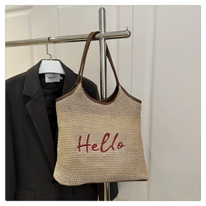 Macro detail of beige woven tote bag featuring red Hello embroidery and leather straps
