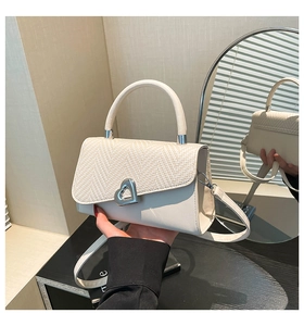 Detail view of beige crossbody bag with V-weave texture and silver heart lock via mirror