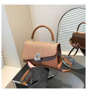 Detail showing straw woven flap and heart-shaped metal lock on a brown leather handbag