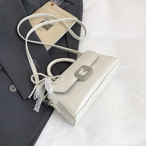 Detail of white leather handbag with silver G-buckle, pearl charm and lace decor