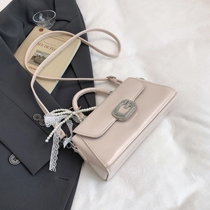 Detail of beige handbag featuring silver G buckle, pearl charm and white lace trim decor