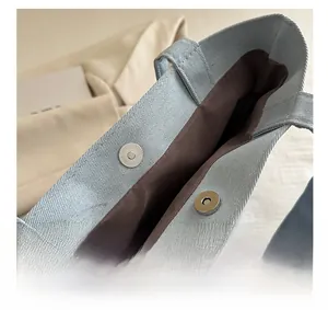 Detail view of the secure silver magnetic buckle closure on a light blue canvas tote bag
