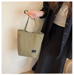 Detail of light green nylon crossbody bag with black rectangular brand logo label