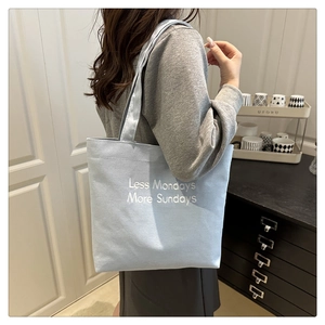 Detail of light blue canvas tote bag featuring white Less Mondays More Sundays text