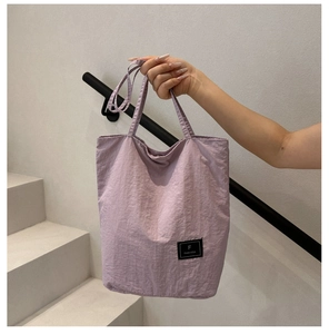 Detail of light purple nylon tote bag featuring a black brand logo patch and long handle