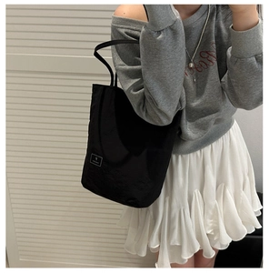 Side view of a black nylon crossbody bag styled with a casual outfit against a white wall