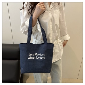Detailed close-up of navy blue denim tote bag featuring white embroidery text detail