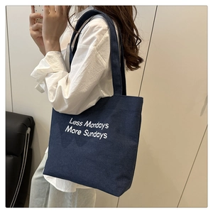 Close-up of navy canvas tote bag featuring embroidered Less Mondays More Sundays text