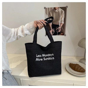 Close-up of black canvas tote bag with 'Less Mondays More Sundays' white embroidery detail