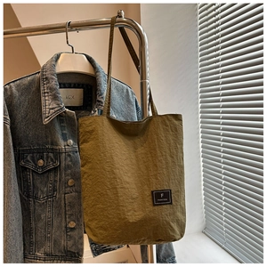 Detail of olive green nylon tote bag with unique crinkle texture and brand logo patch