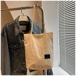 Detail of off-white wrinkled nylon tote bag with black square logo on steel hanger