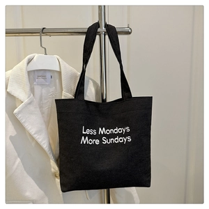 Detail of black canvas tote bag with white Less Mondays More Sundays embroidery