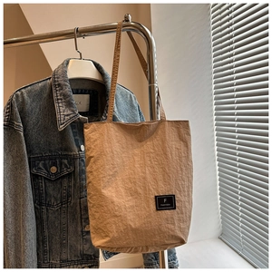 Detail of beige nylon tote bag featuring brand label and crinkle texture fabric surface
